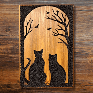 A carving in recycled wood shows a silhouette of two cats watching birds flying between nearby trees.